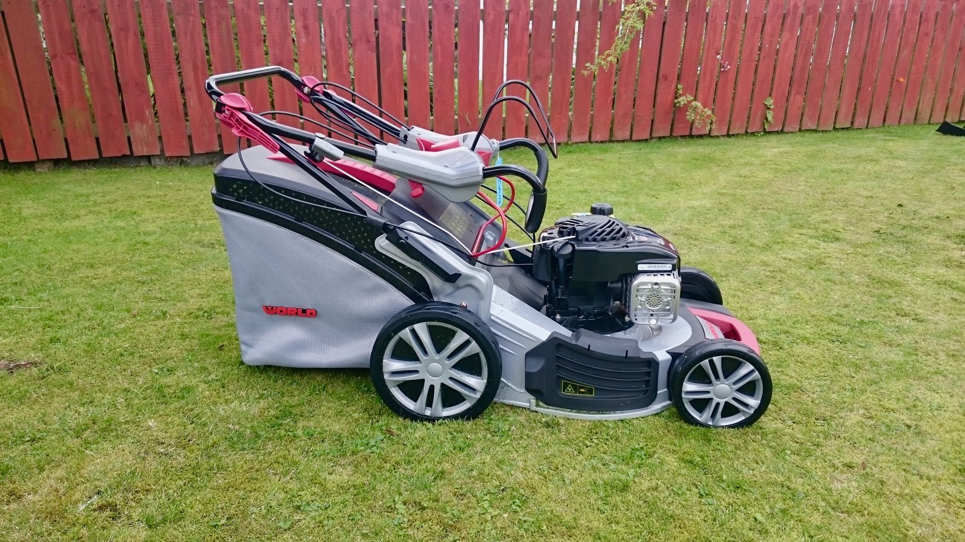 Photograph of a World brand, petrol engined, rotary lawnmower, with folded handles. 
