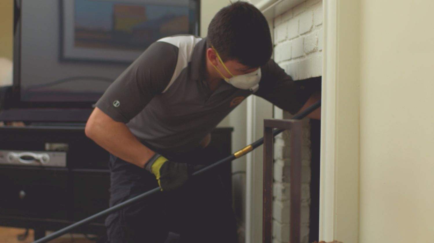 A man wearing a mask and gloves is cleaning a fireplace with a broom.