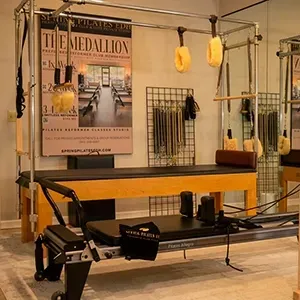 Pilates reformer machine with yellow bench in a studio, hanging straps, and wall poster.