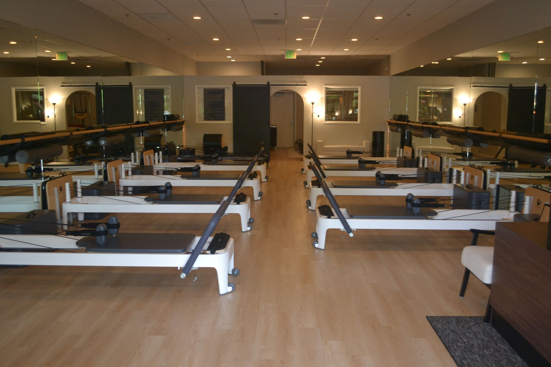 Pilates reformer machine with yellow bench in a studio, hanging straps, and wall poster.