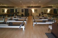 Pilates reformer machine with yellow bench in a studio, hanging straps, and wall poster.