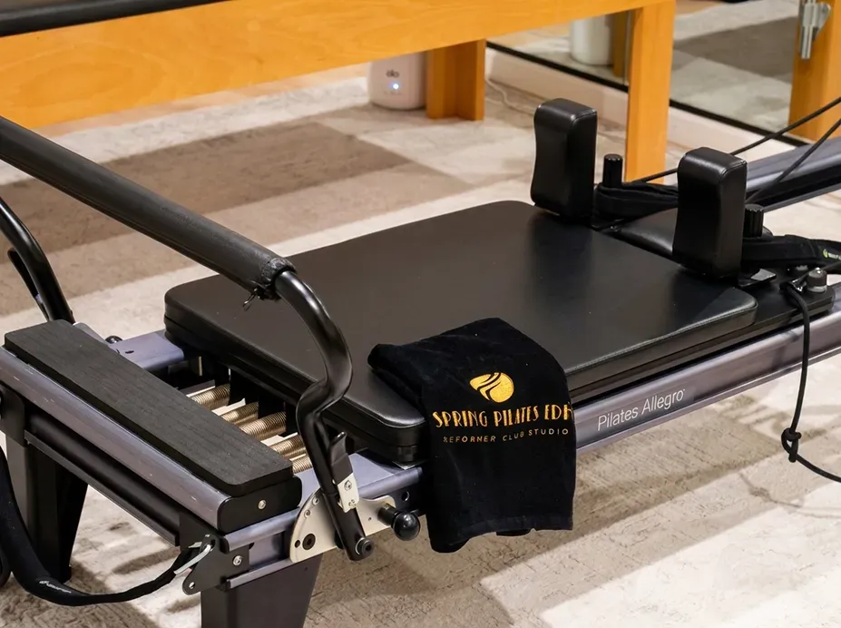Black exercise machine on a carpeted floor beside a wooden table, with a black cloth hanging over it.