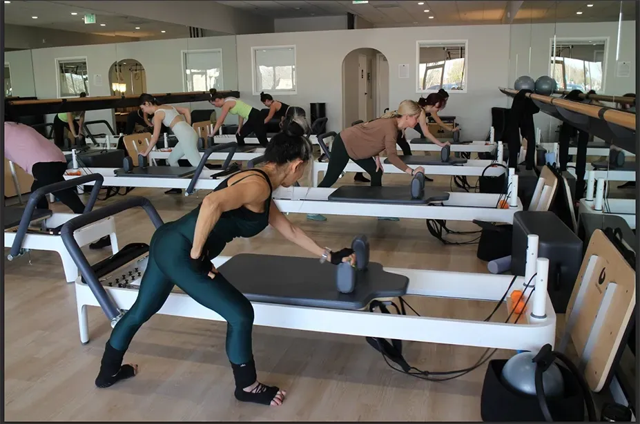 People exercising on reformer Pilates machines in a mirrored studio