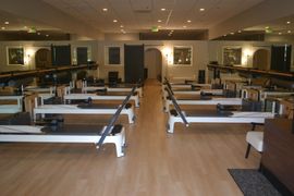 Pilates reformer machine with yellow bench in a studio, hanging straps, and wall poster.