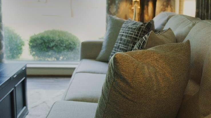 A living room with a couch and pillows in front of a window.