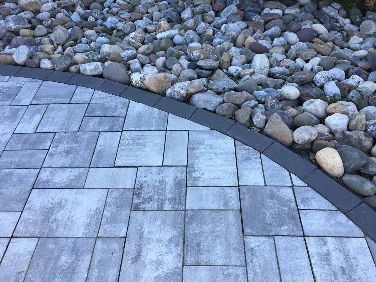 A brick walkway with a black border and rocks on the side.