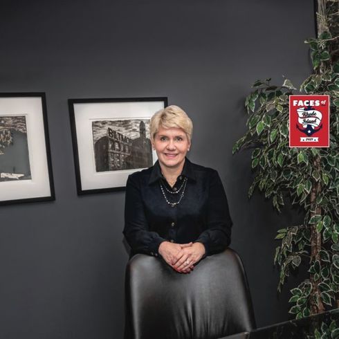 Woman standing behind a chair in a dark office with framed black-and-white art and a red sign on the wall