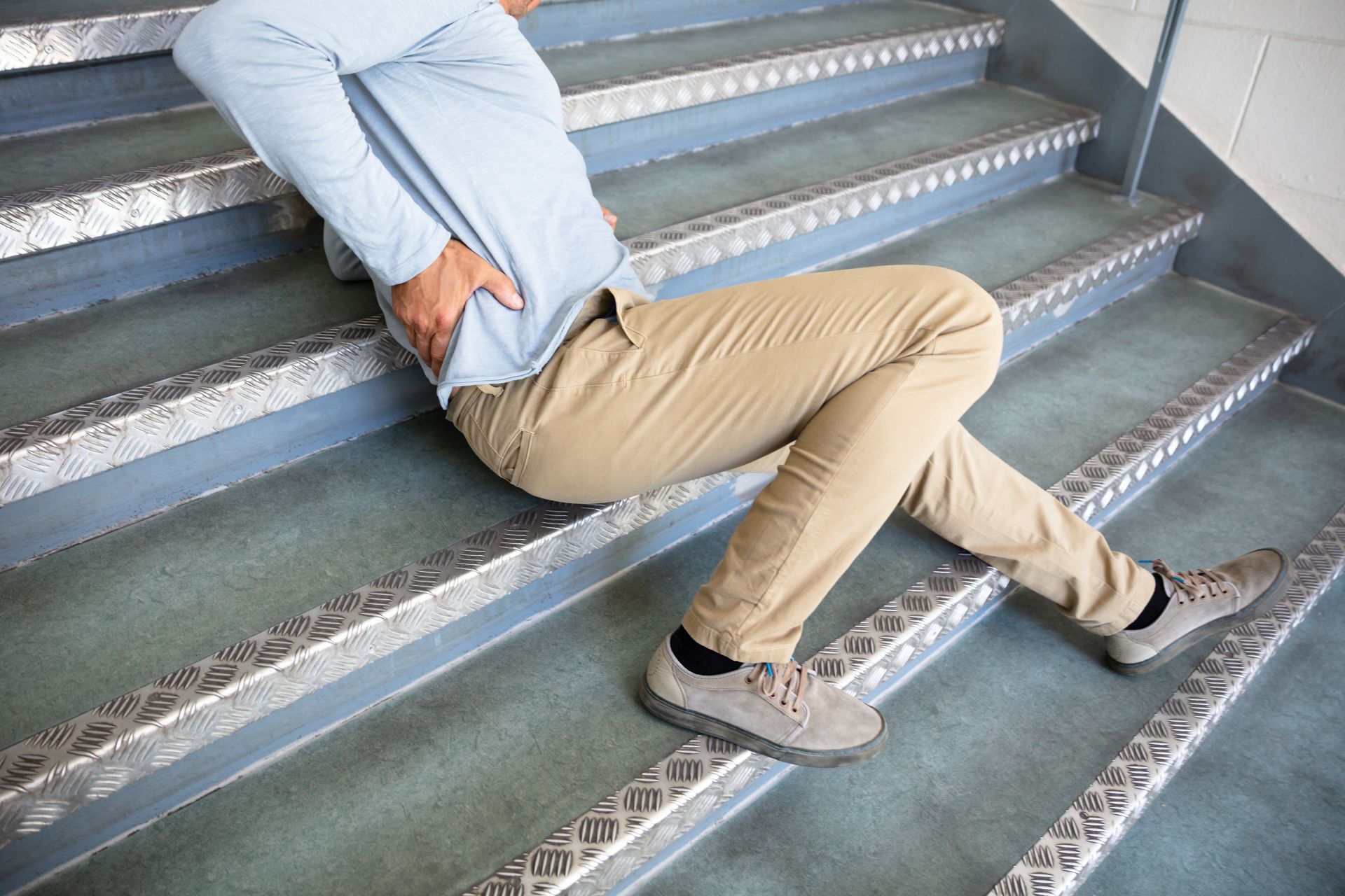 Person sitting on metal stairs, leaning back and holding their lower back in pain.