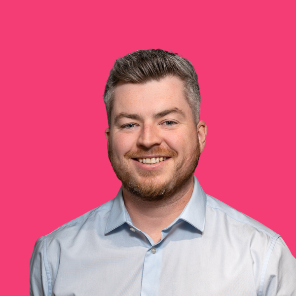 Smiling man in light blue shirt against a bright pink background.