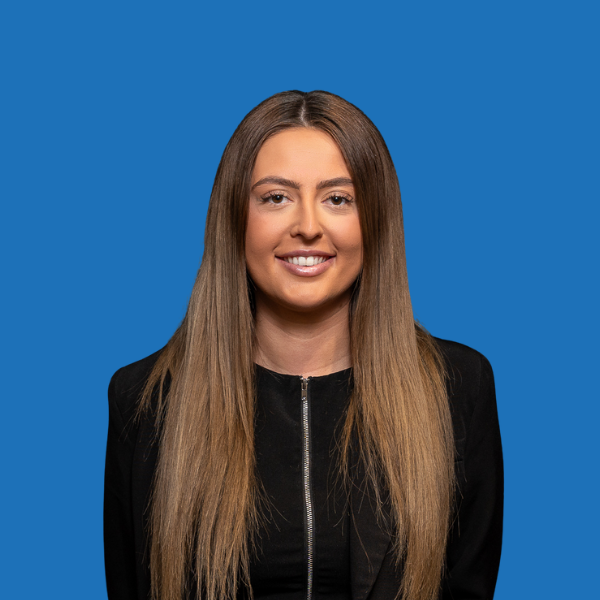 Woman with long brown hair, smiling, wearing a black top against a blue background.