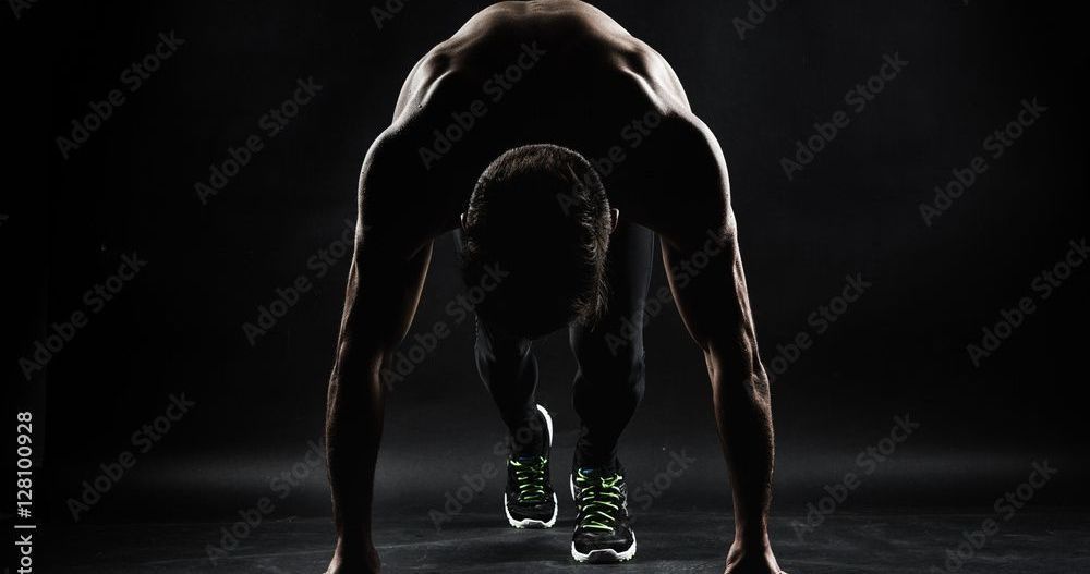 A silhouette of a man getting ready to run in the dark.