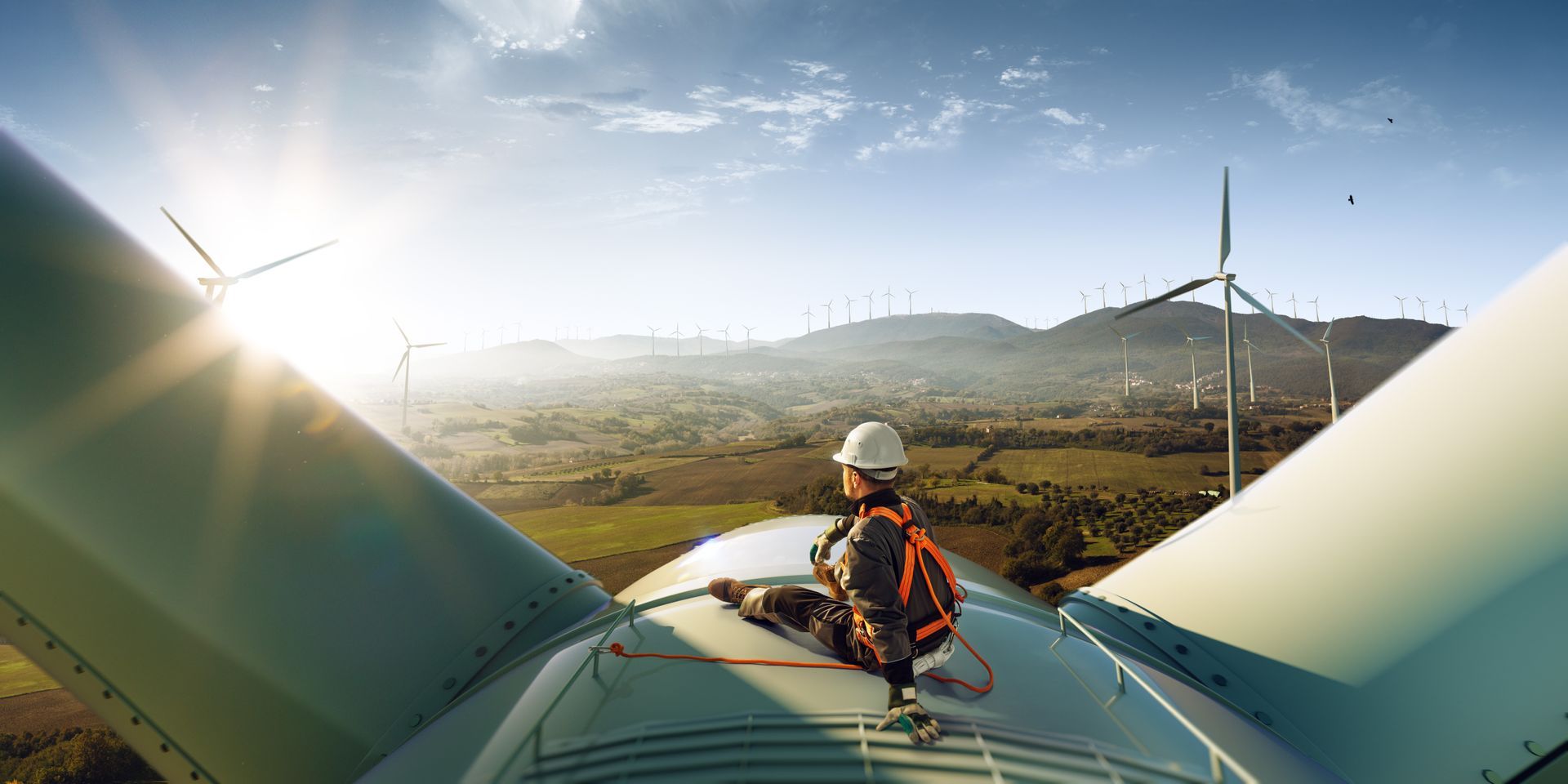 A man is sitting on top of a wind turbine.