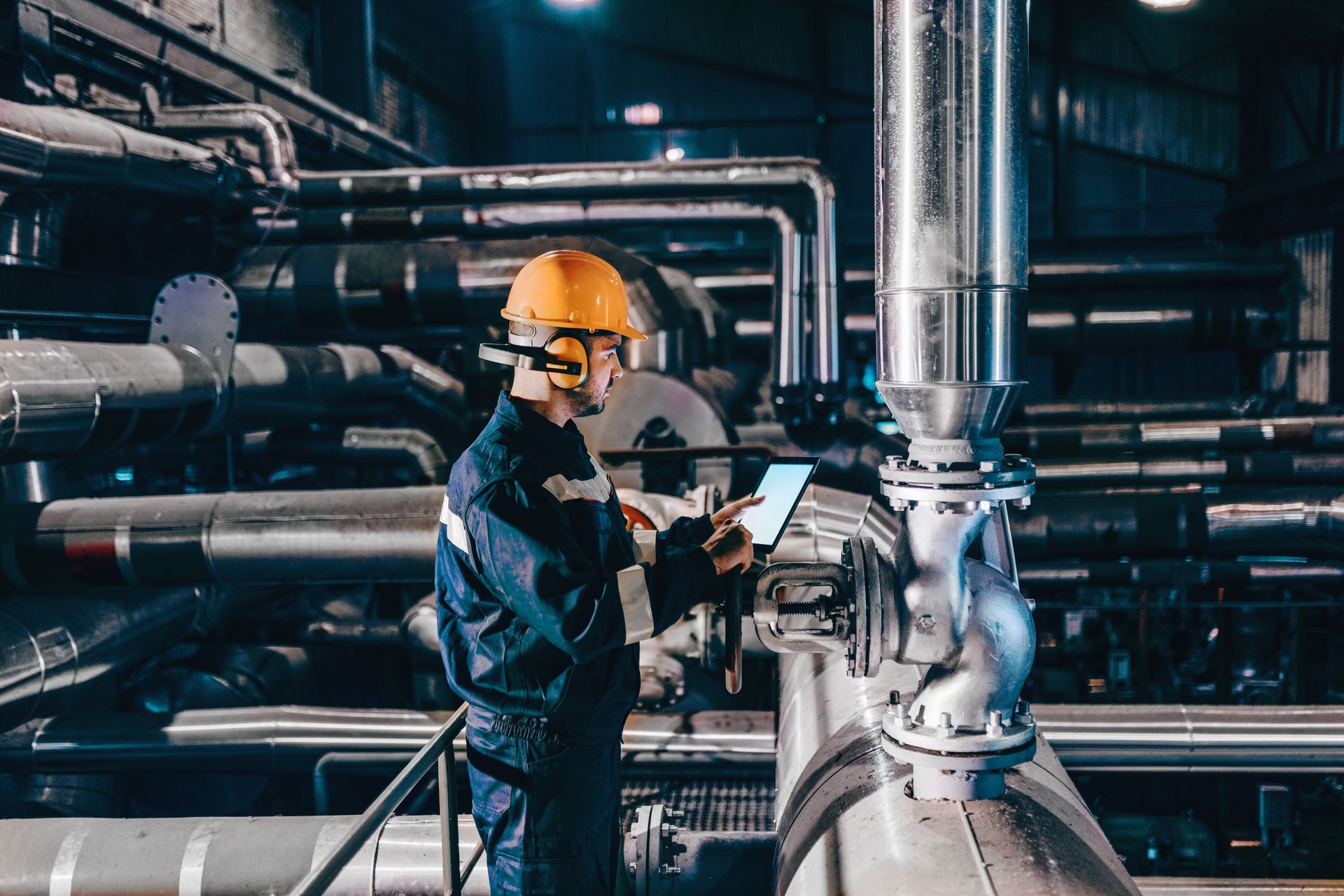 A man in a hard hat is using a tablet in a factory.