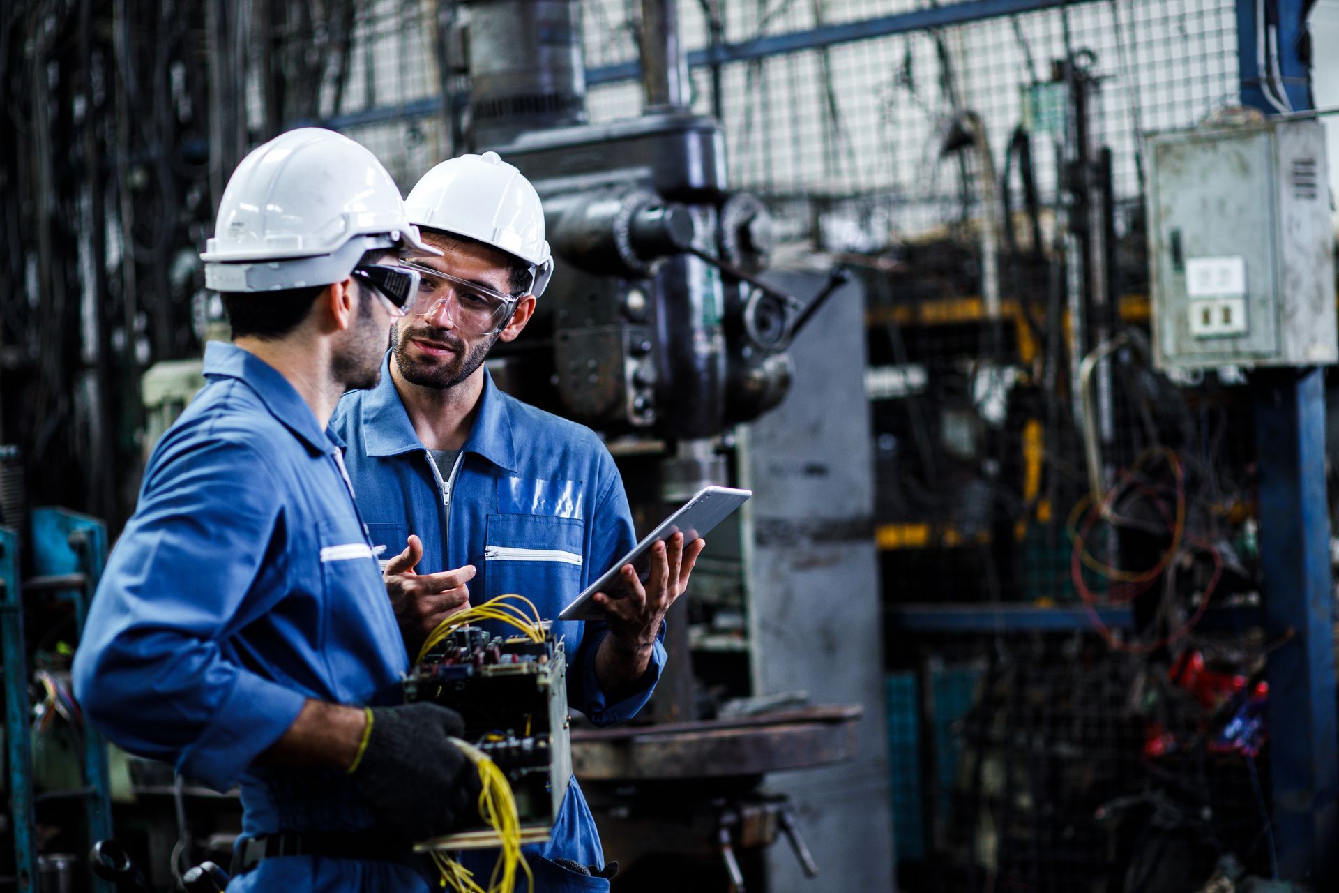 Two men are standing in a factory looking at a tablet.