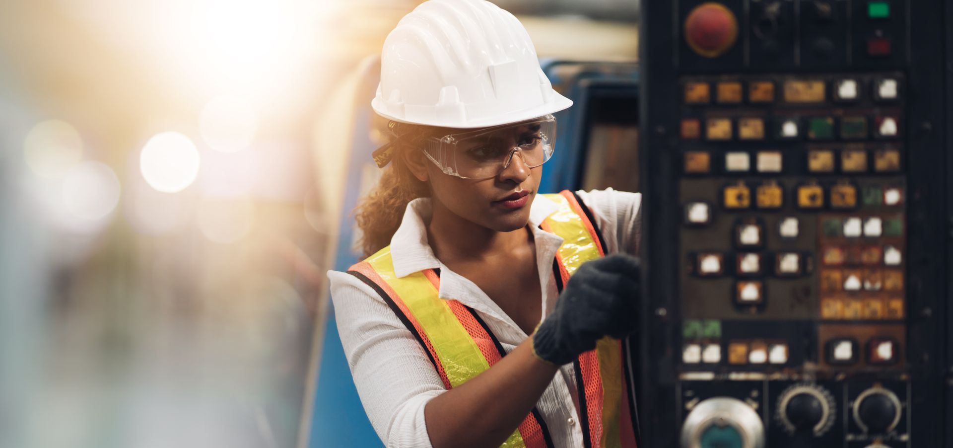 A woman wearing a hard hat and safety vest is working on a machine in a factory.