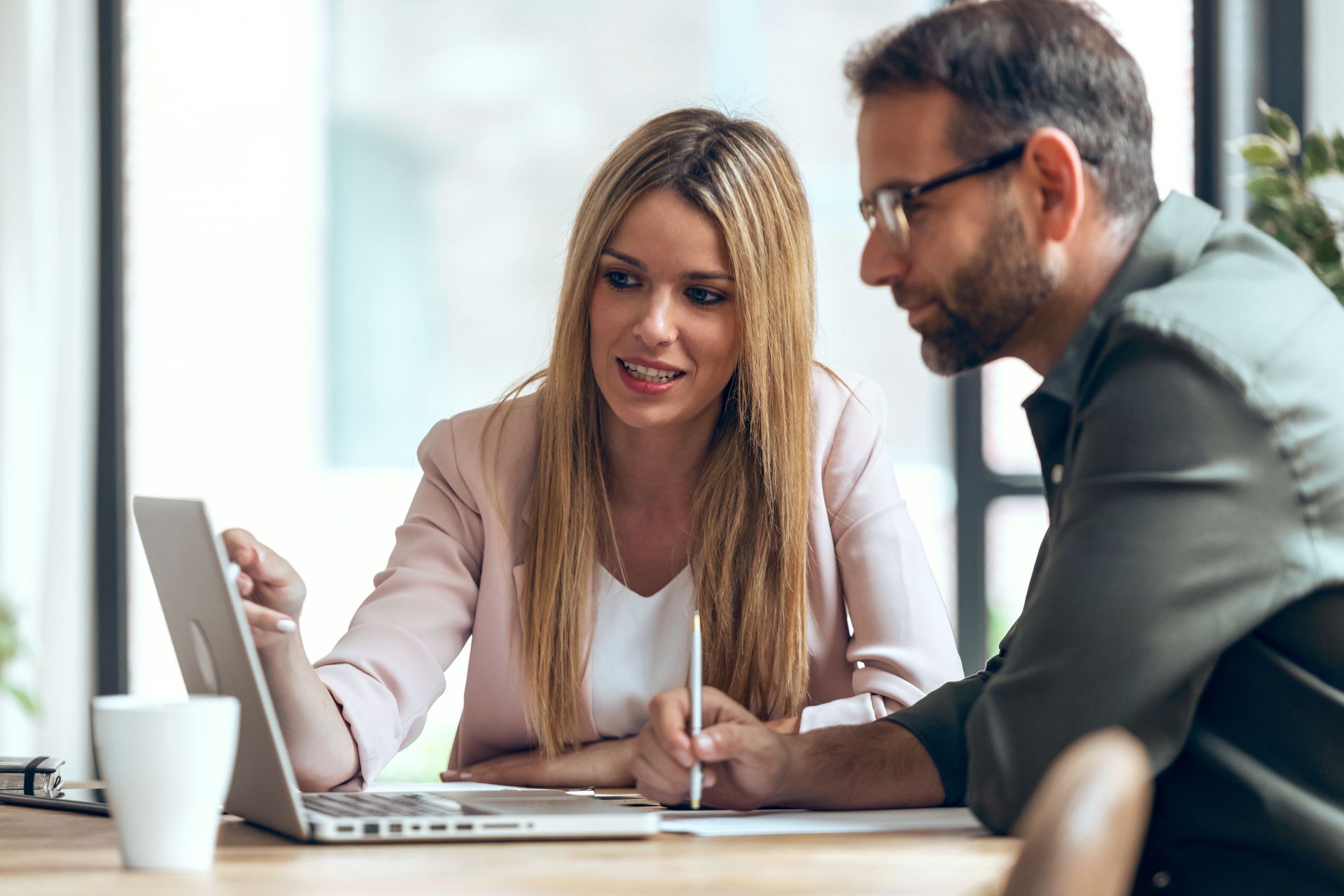 A man and a woman are sitting at a table looking at a laptop.