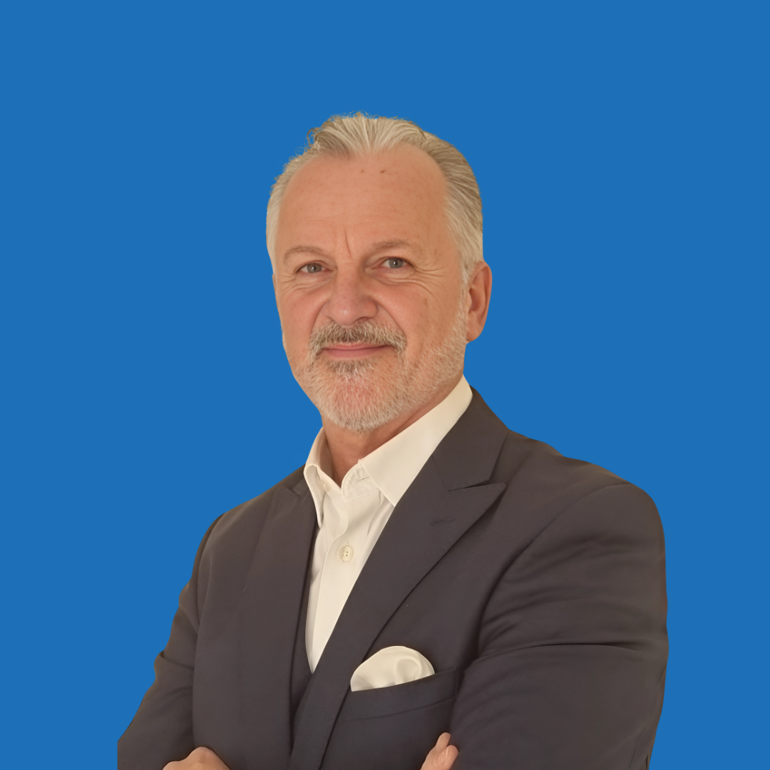 Man in suit, white shirt, and pocket square smiles against a blue background.