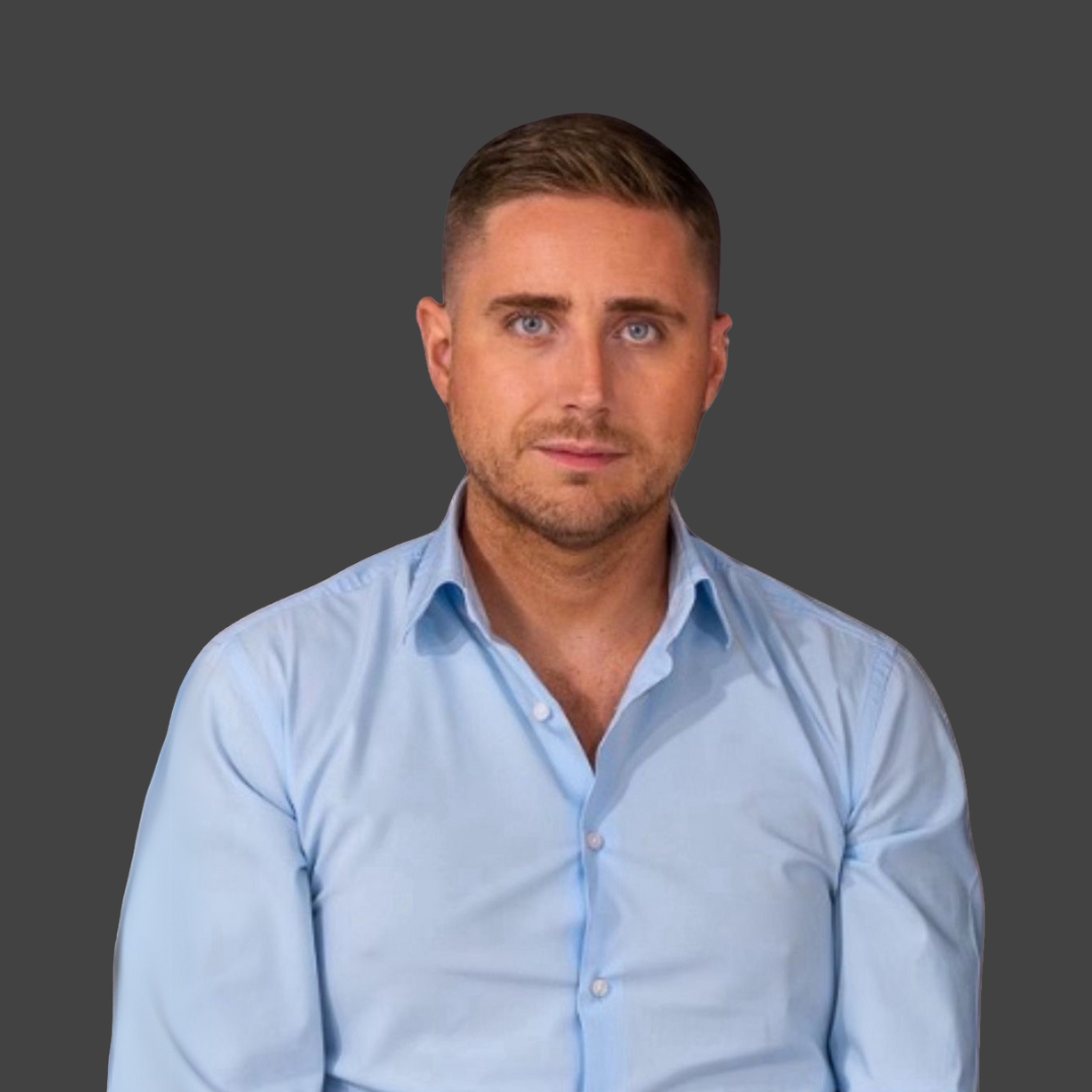 Man in a light blue button-down shirt, looking forward with a neutral expression against a gray background.