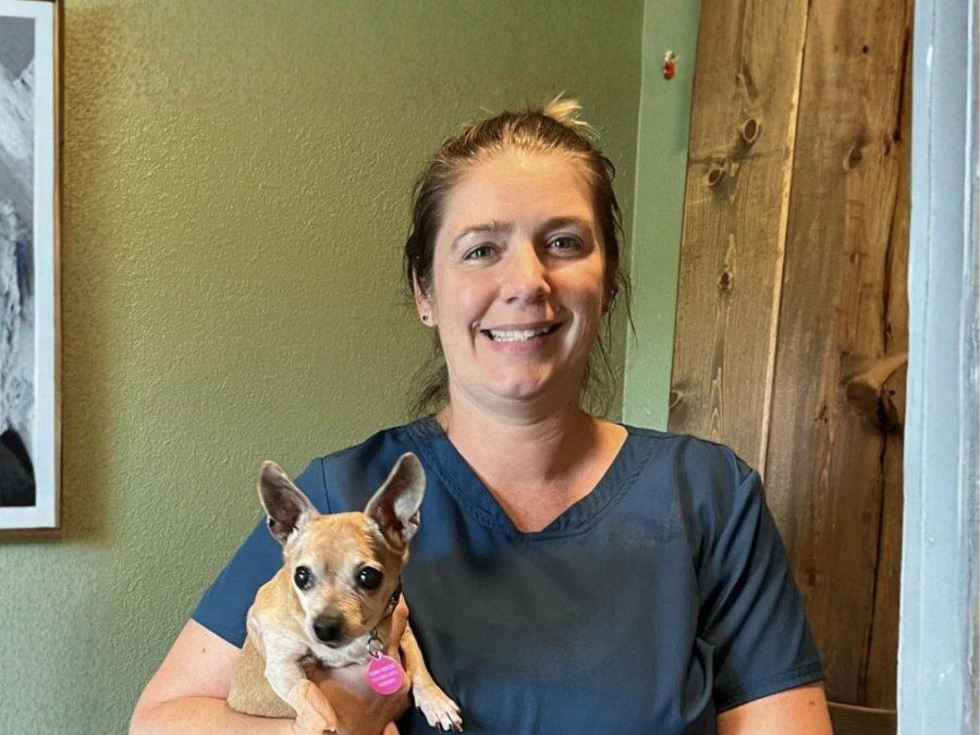 Smiling person holding a small tan dog indoors beside a green wall and wooden door