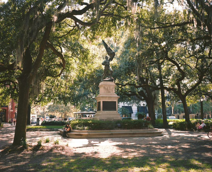 Statue in a shaded city park with large trees and dappled sunlight