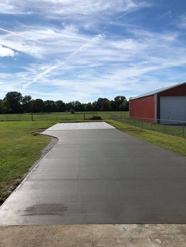 A concrete driveway with a red barn in the background.