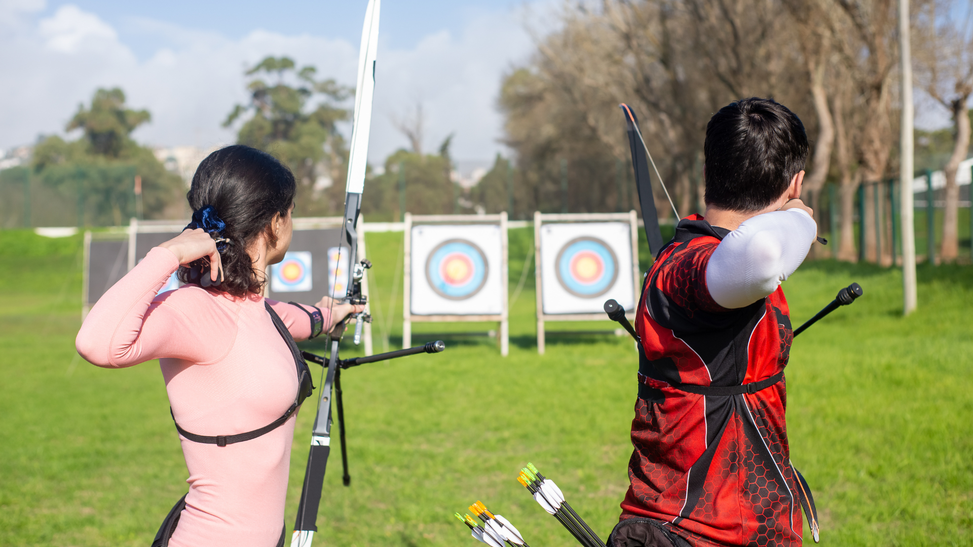 A man and a woman are playing archery in a field.