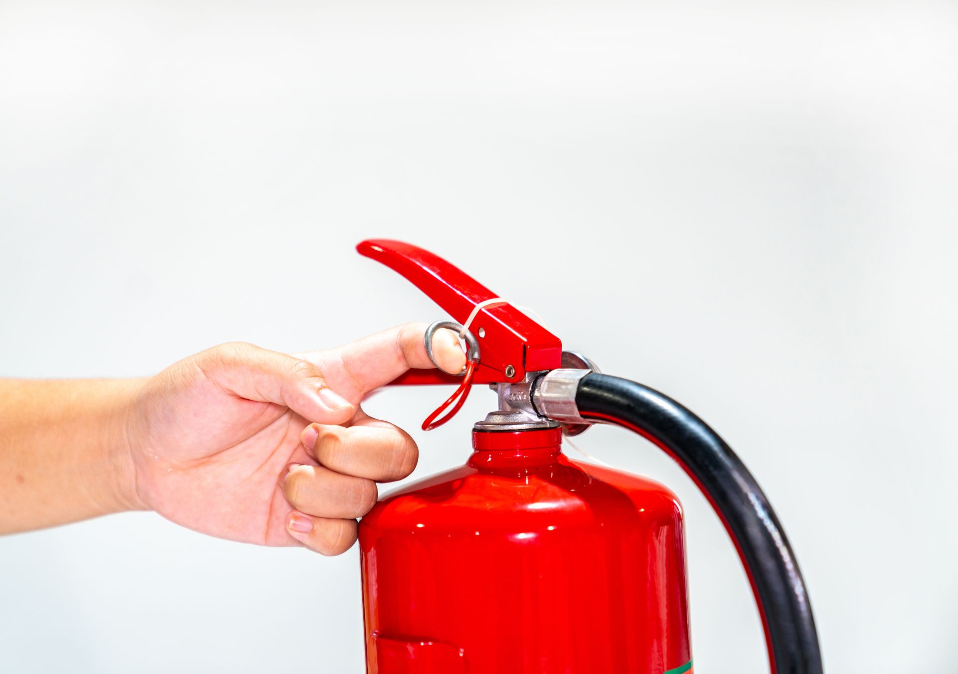 Hand turning a red fire extinguisher handle with a black hose attached