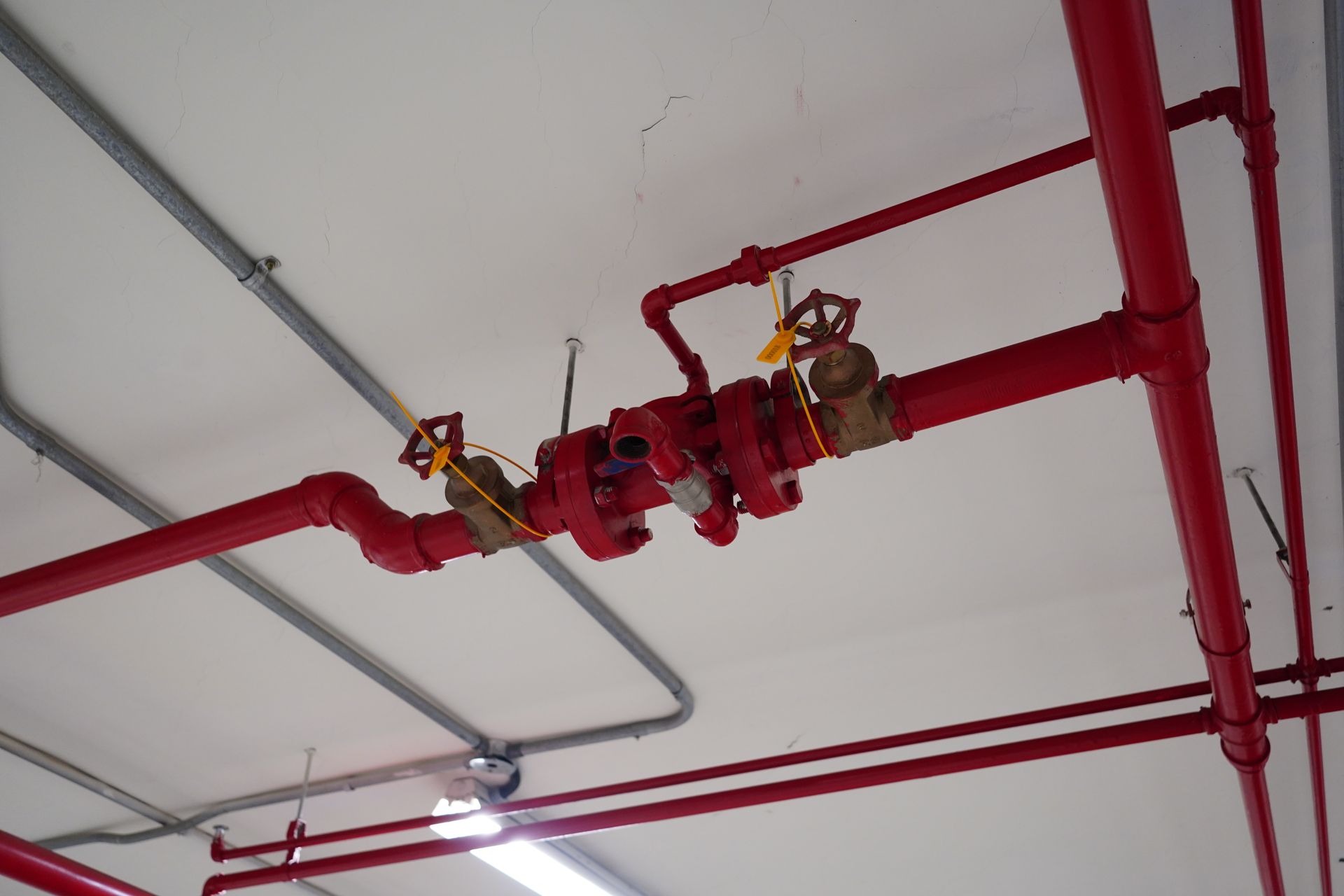 Red fire-sprinkler piping and valves on a white ceiling in an industrial interior Red fire-sprinkler piping and valves on a white ceiling in an industrial interior