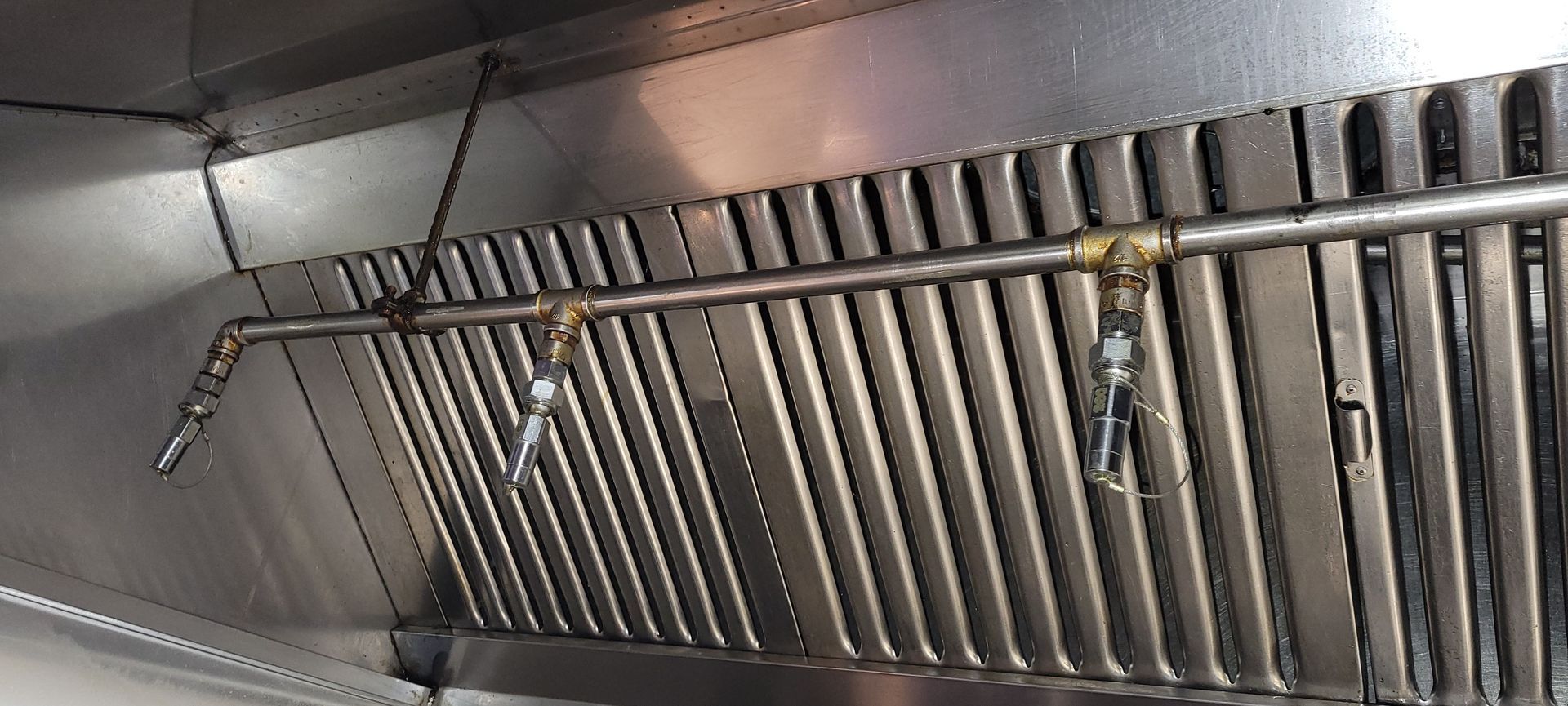 Stainless steel pipes and valves mounted on a corrugated metal wall inside an industrial facility