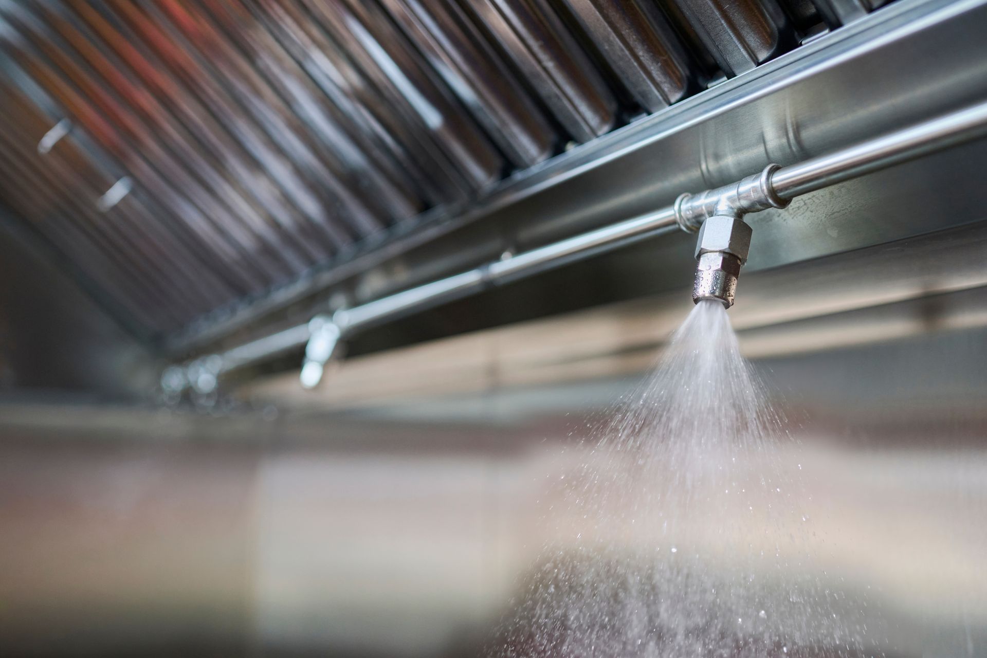 Sprinkler nozzle spraying water beneath a metal ceiling in a commercial kitchen Sprinkler nozzle spraying water beneath a metal ceiling in a commercial kitchen