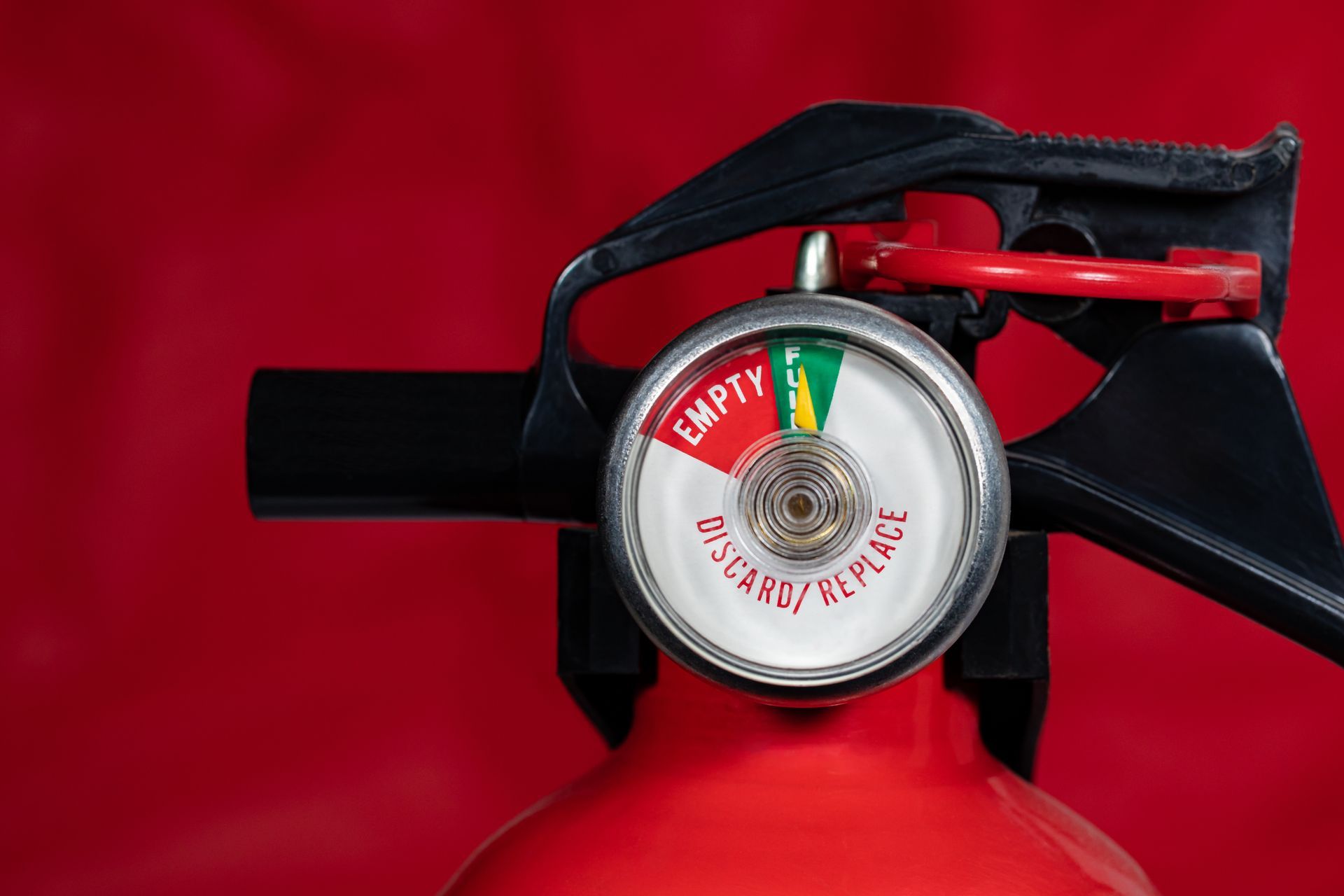 Fire extinguisher close-up against a red background, showing the pressure gauge and handle. Fire extinguisher close-up against a red background, showing the pressure gauge and handle.