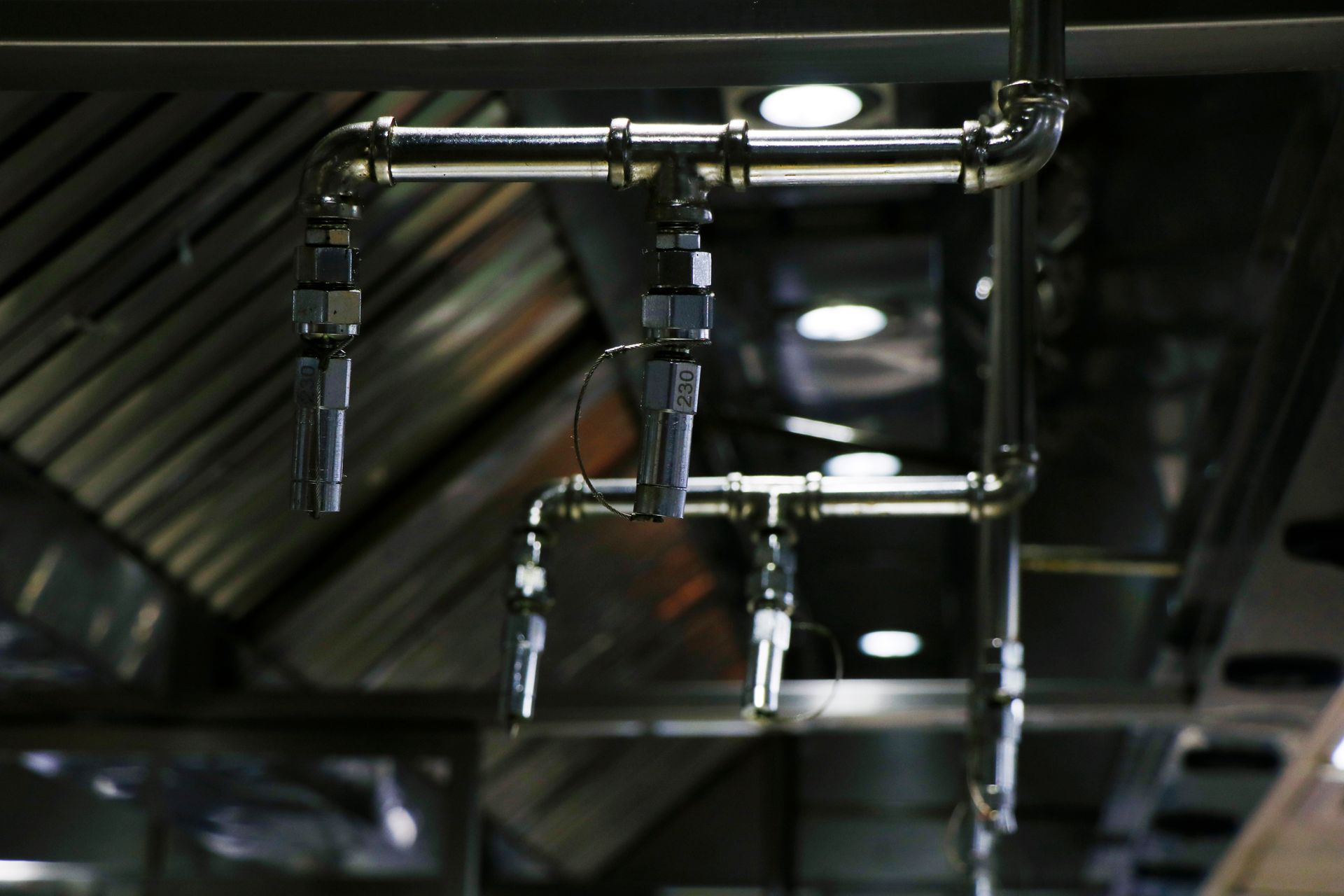 Industrial piping and valves on a dark ceiling with overhead lights