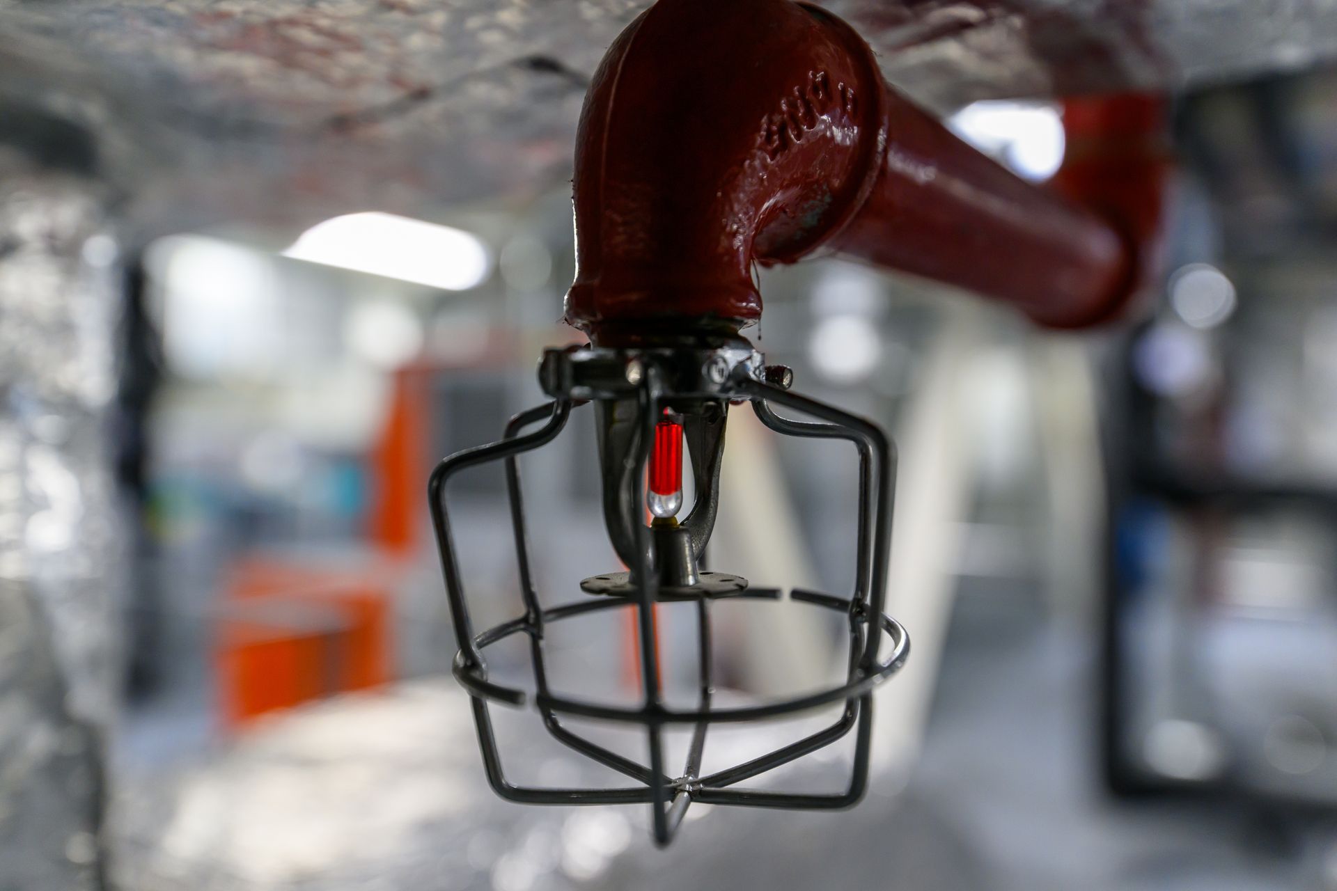 Red fire sprinkler head with wire cage in an industrial interior, blurred background