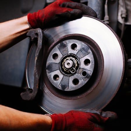 Hands wearing red gloves holding a car brake rotor and caliper.