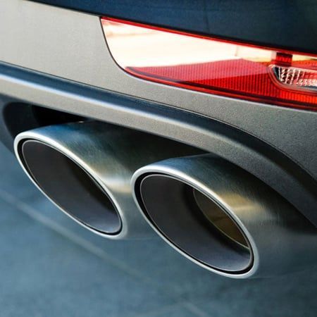 Close-up of a car's exhaust pipes and tail light; silver pipes, black trim, gray car.