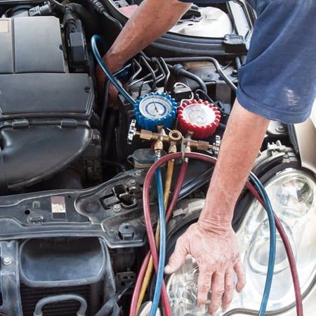 Mechanic working on car engine, attaching gauges for AC service.