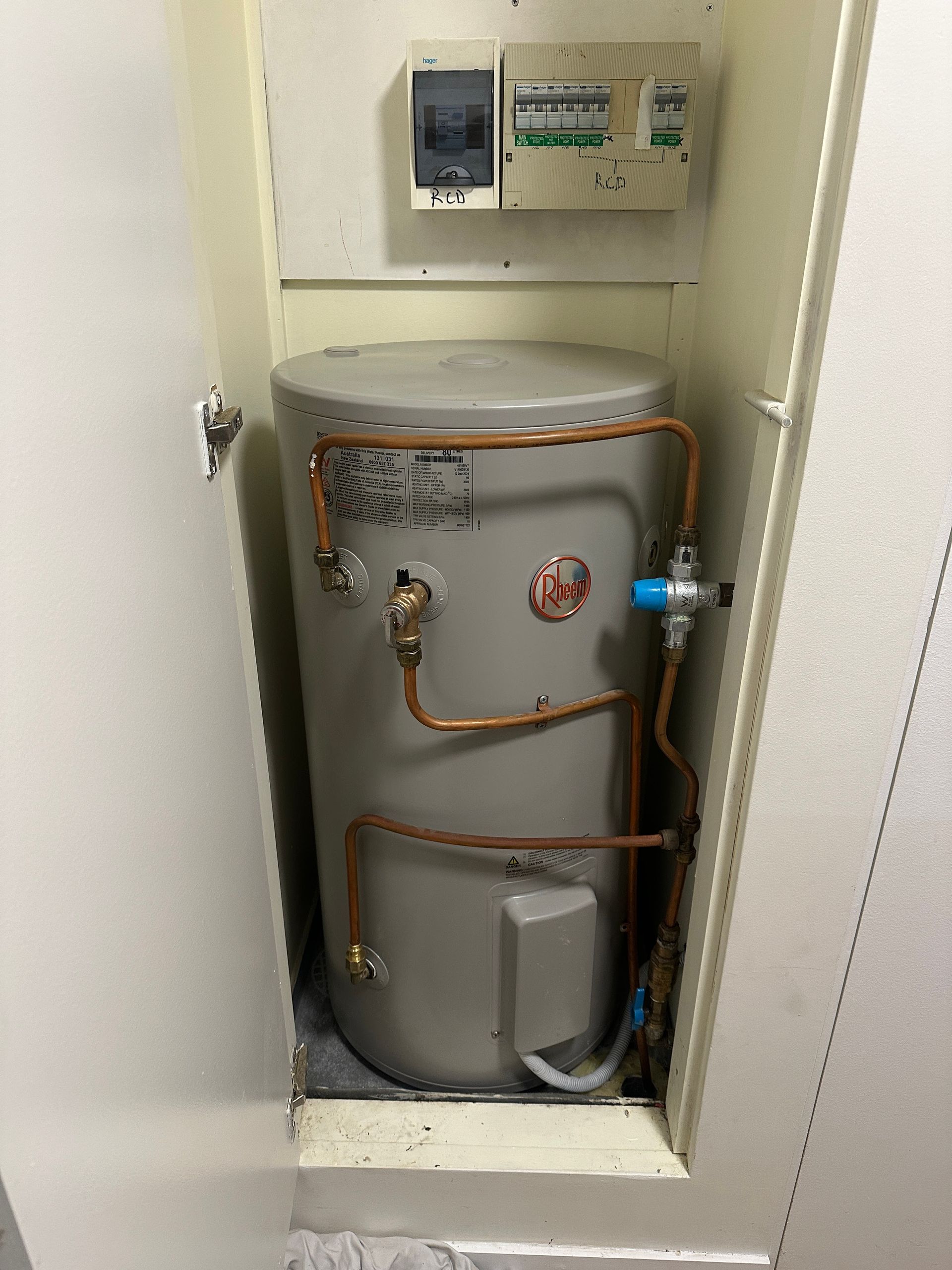 A Hot Water Heater in a Cabinet With Copper Pipes and Electrical Panel — Vantage Plumbing and Drainage In Helensvale, QLD