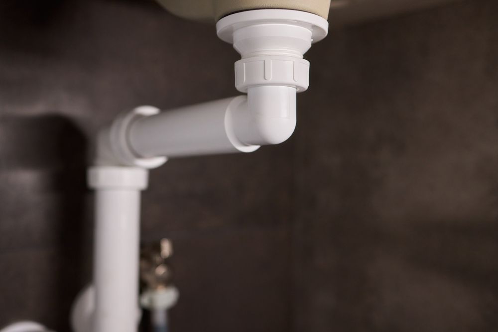 White plumbing pipes under a sink. Elbow joint and vertical drain pipe visible. — Vantage Plumbing and Drainage In Mudgereeba, QLD