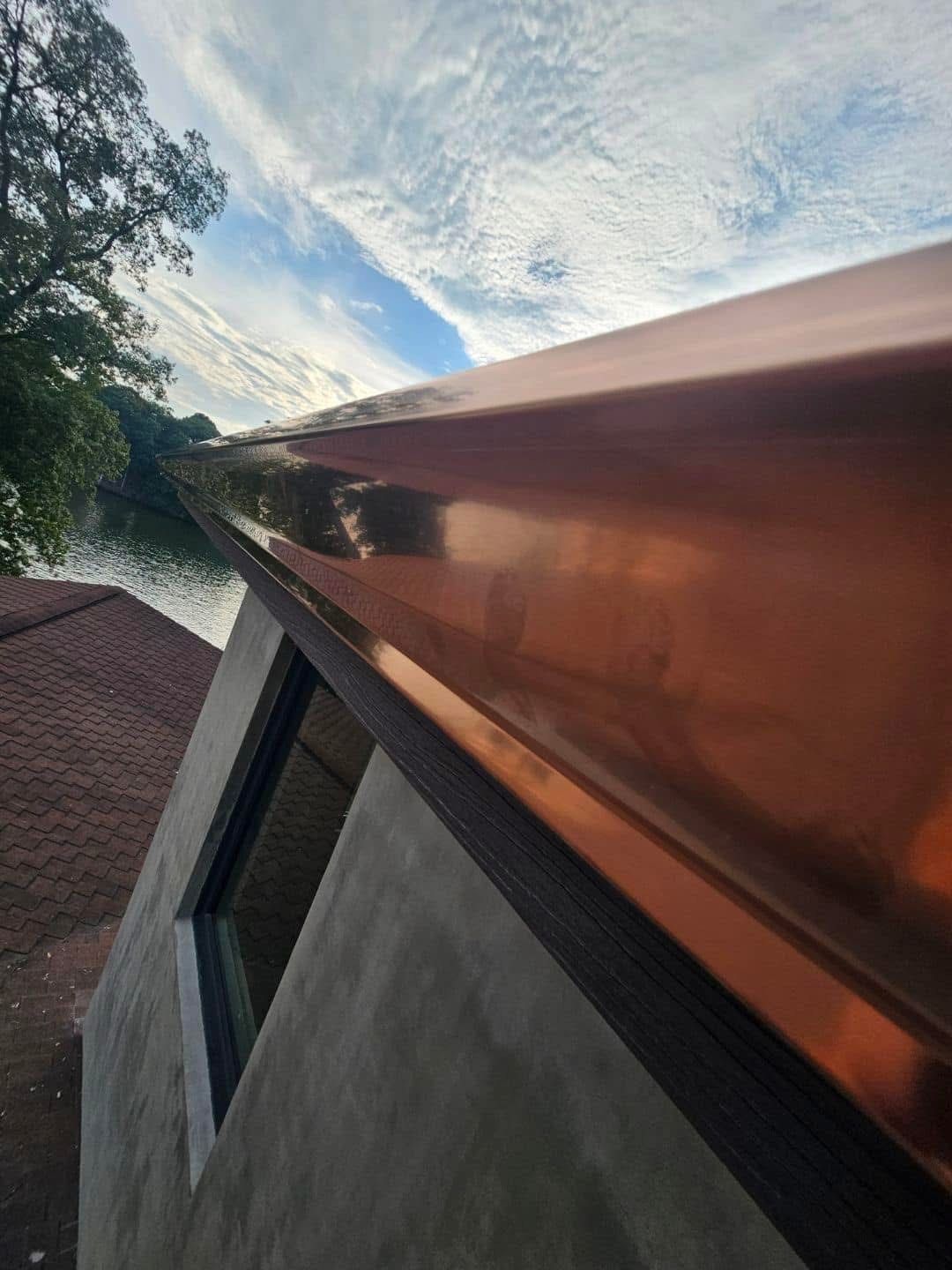 Copper-colored roofing, against a cloudy sky, over a house with a window.