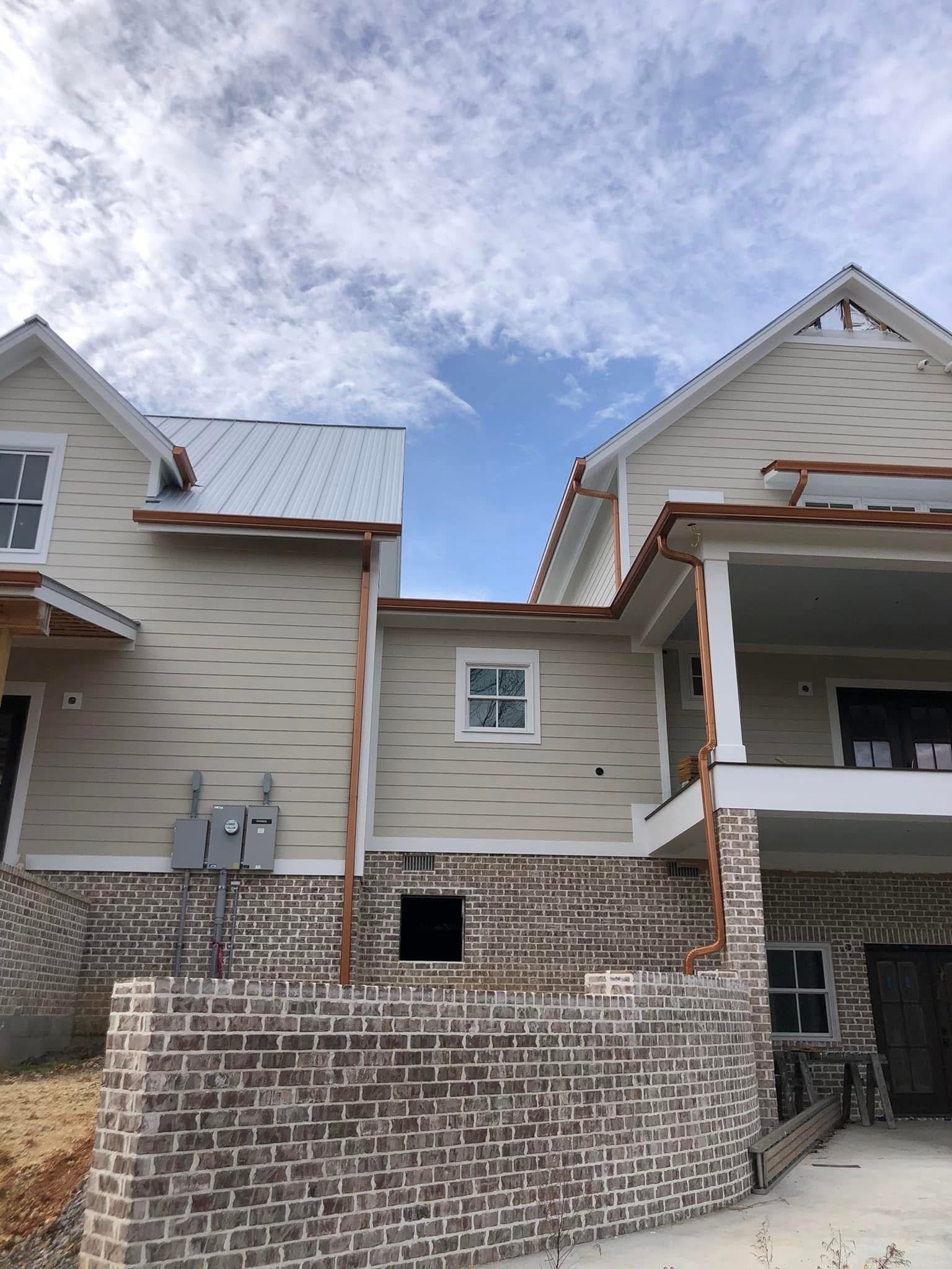 Townhouses under construction, beige siding, copper gutters, brick foundation, cloudy sky.