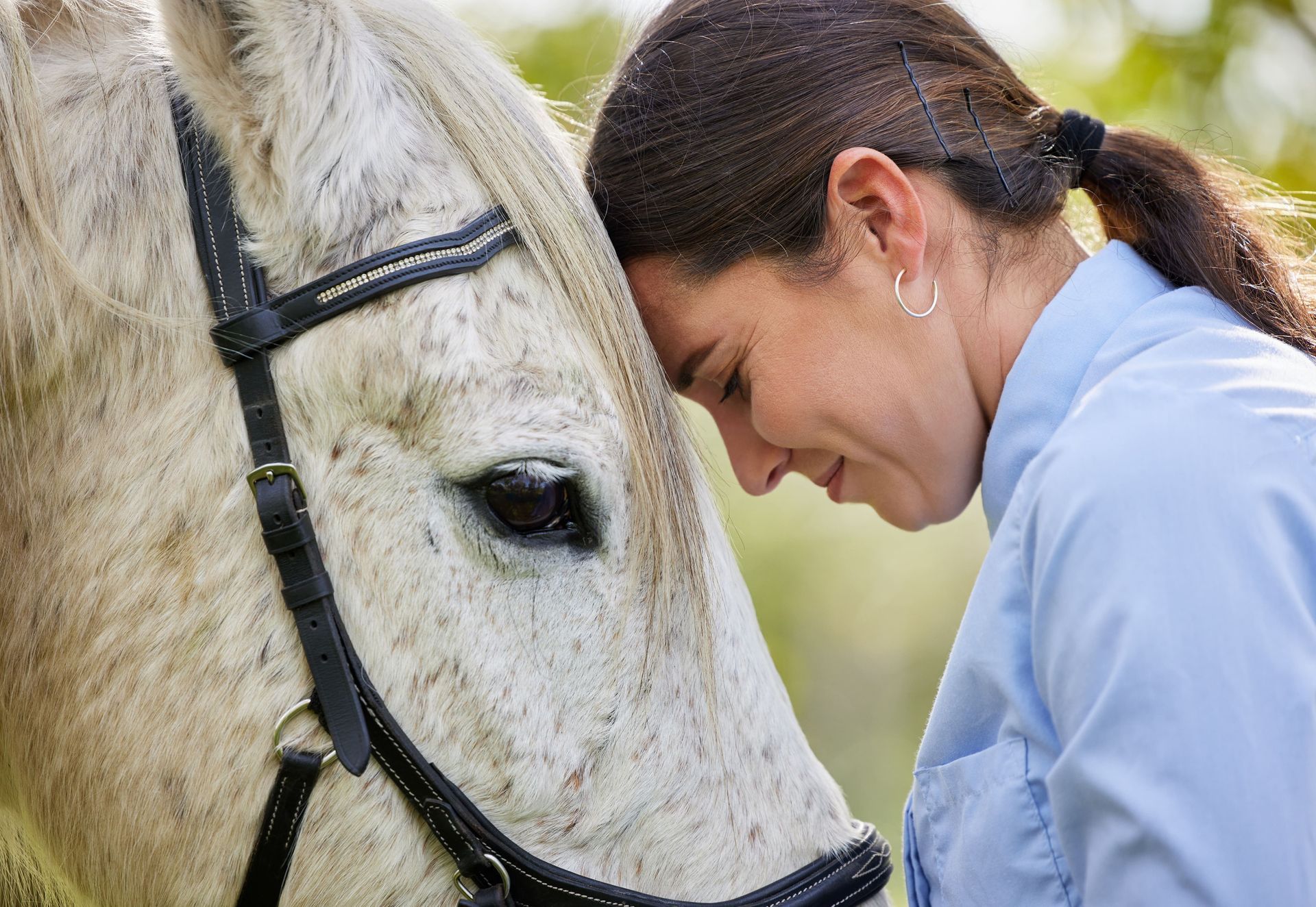 A woman is leaning her head on a white horse 's head.