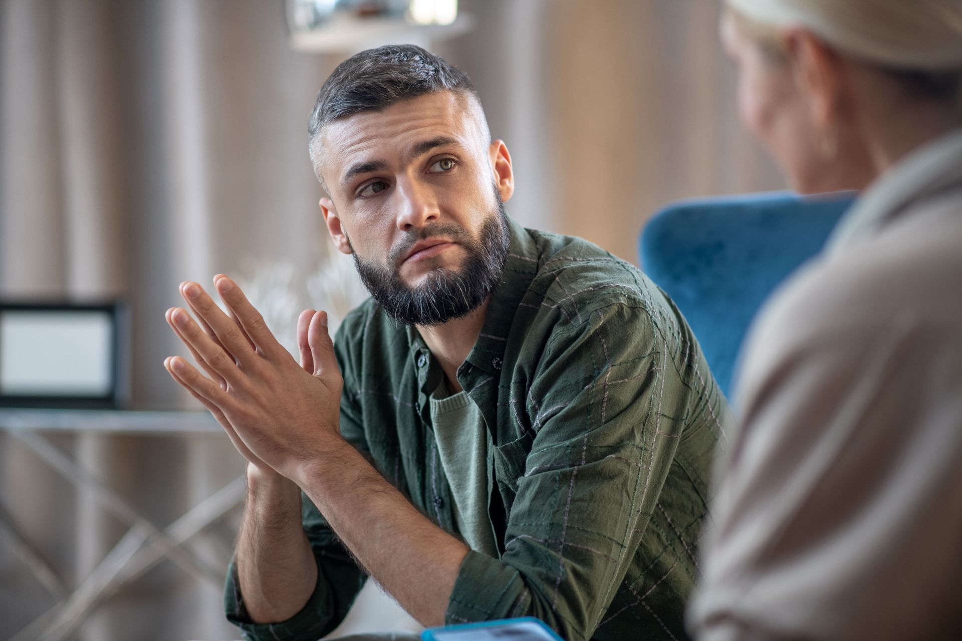 A man with a beard is sitting in a chair talking to a woman.