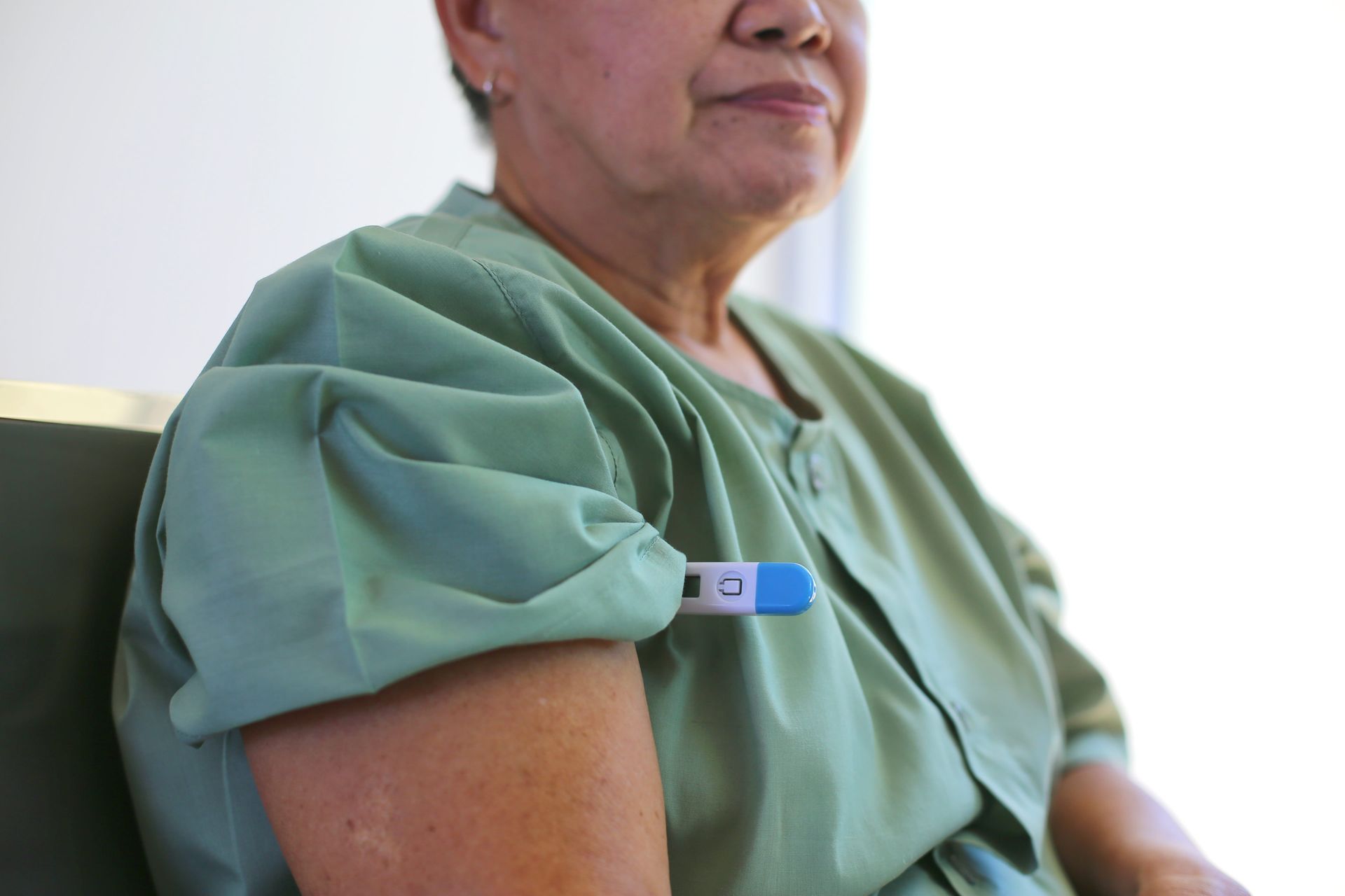 A woman in a hospital gown has a thermometer on her arm.