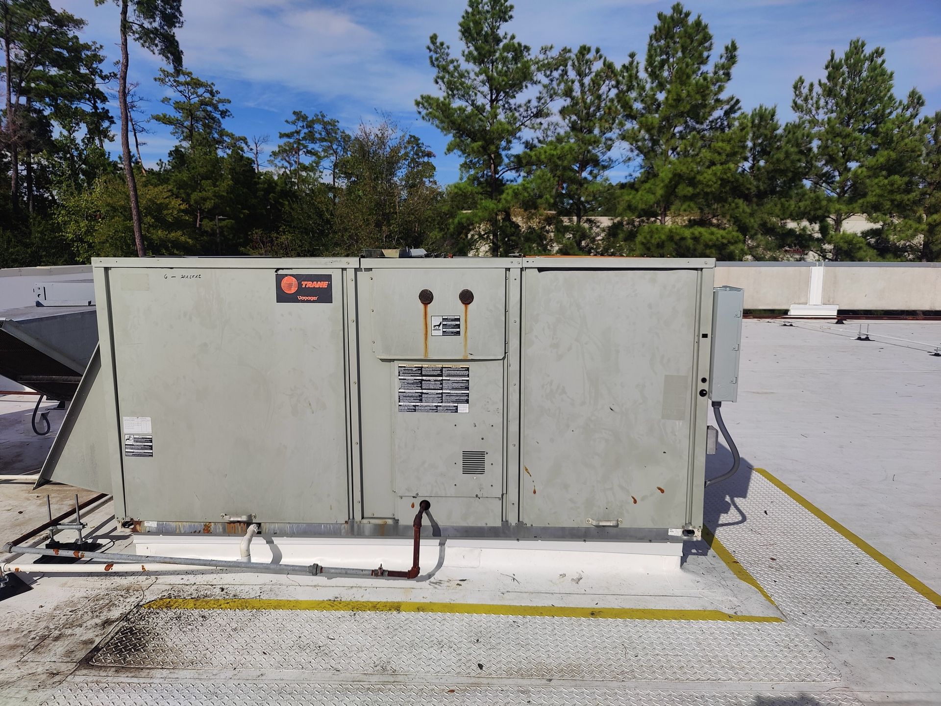 Rooftop HVAC unit on a building, gray metal with warning labels, surrounded by white sealant and a yellow platform.