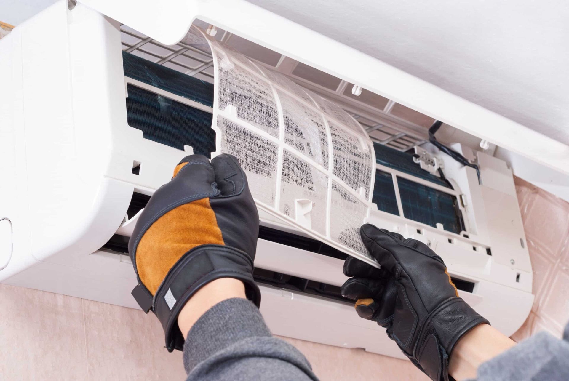 Person wearing gloves removing an AC unit filter for cleaning.