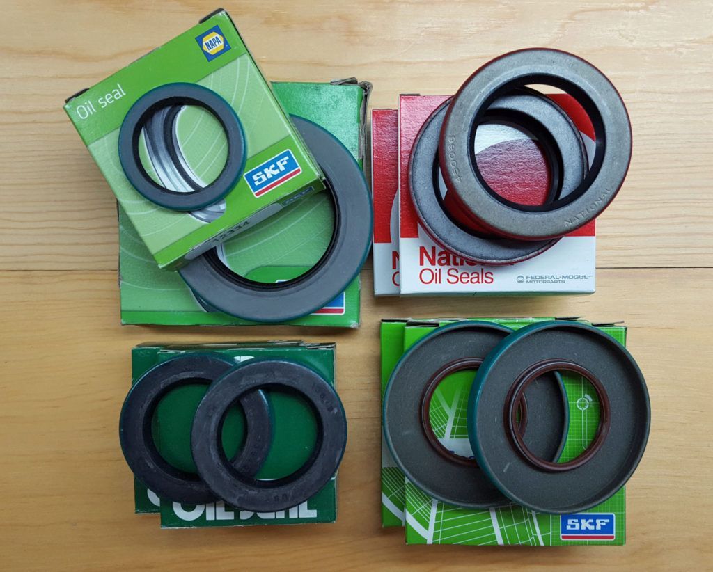 Four sets of SKF oil seals with green and red packaging on a wooden surface. The seals are circular and dark in color.