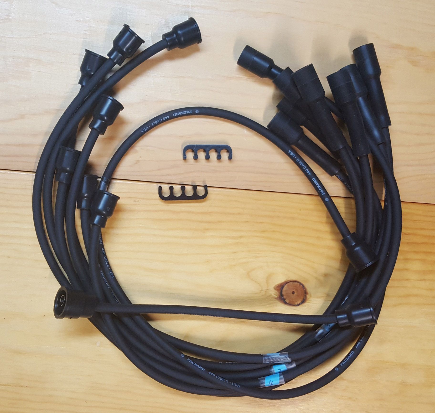 Black spark plug wires, two wire separators, and a small wooden disc on a wooden surface.