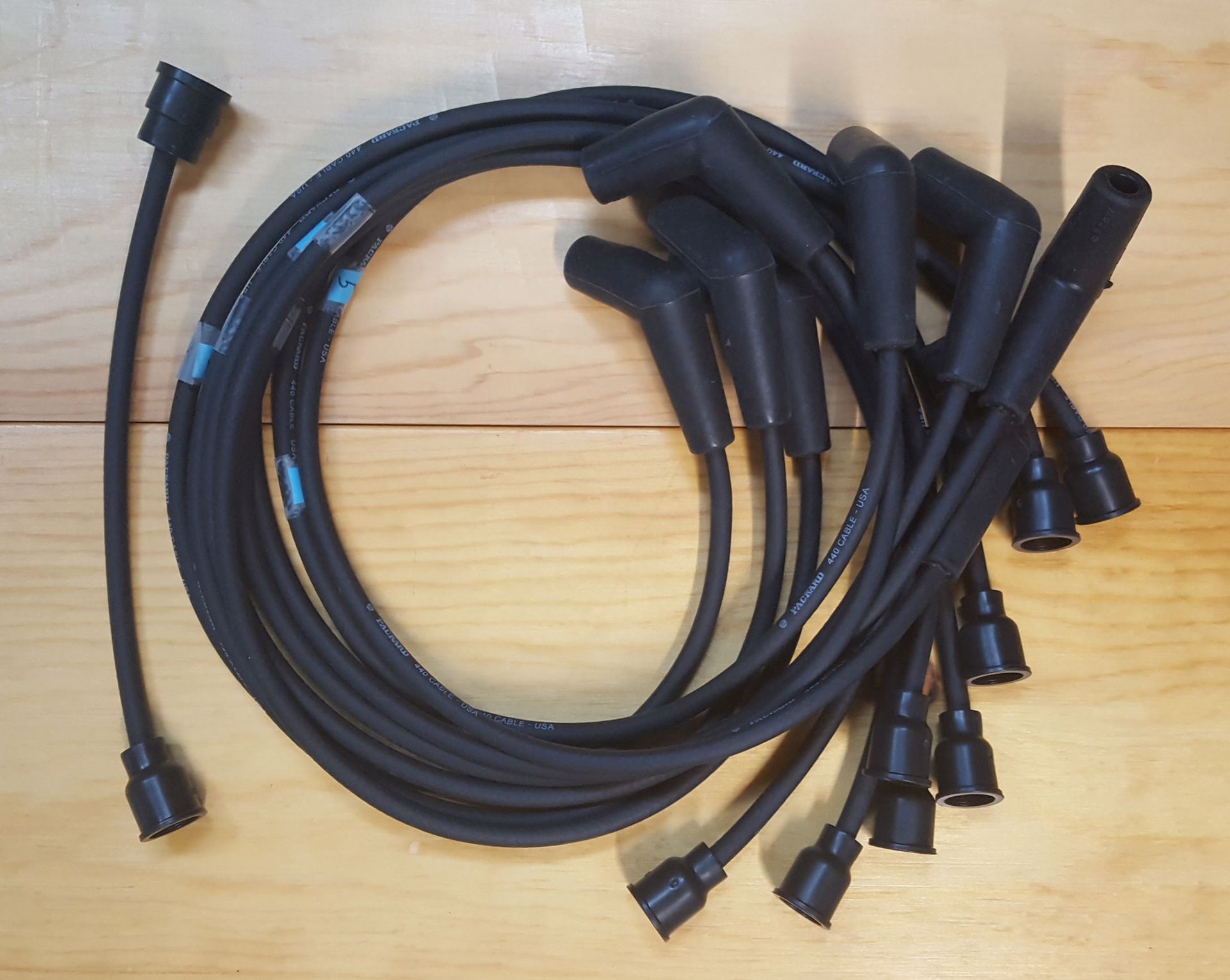Black spark plug wires coiled on a wooden surface, featuring several angled boots and connector ends.