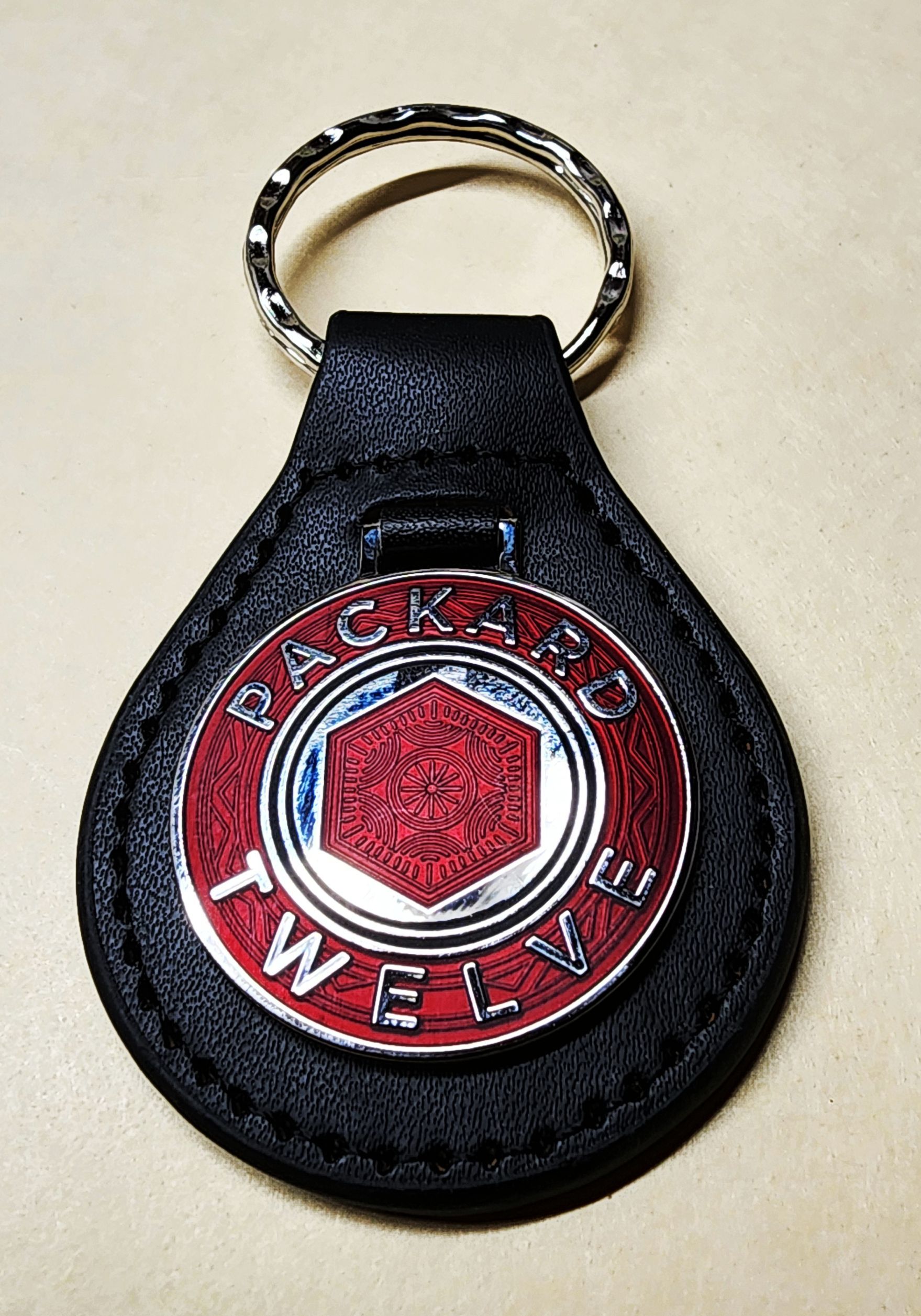 Black leather key fob with a silver ring. The fob has a decorative silver emblem with the text 