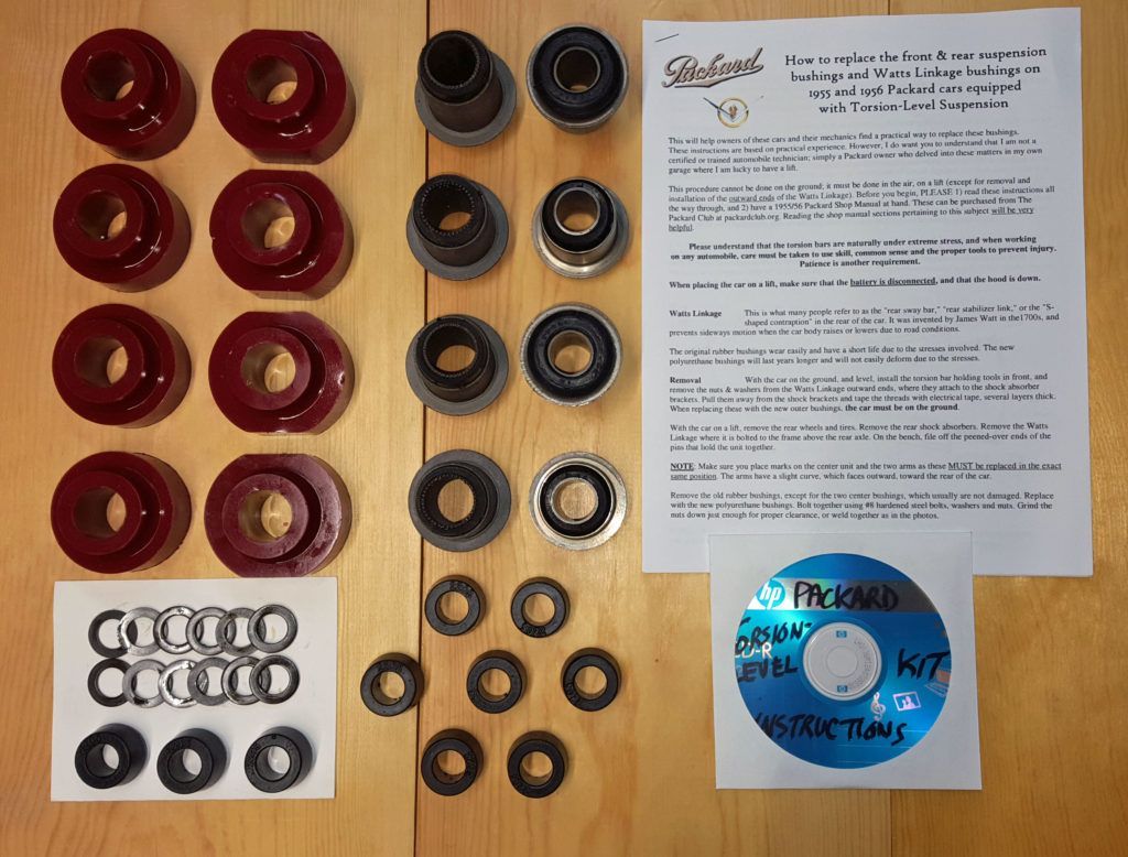 A collection of red, silver, and black car parts laid out on a wooden surface, alongside a paper with text and a blue CD.